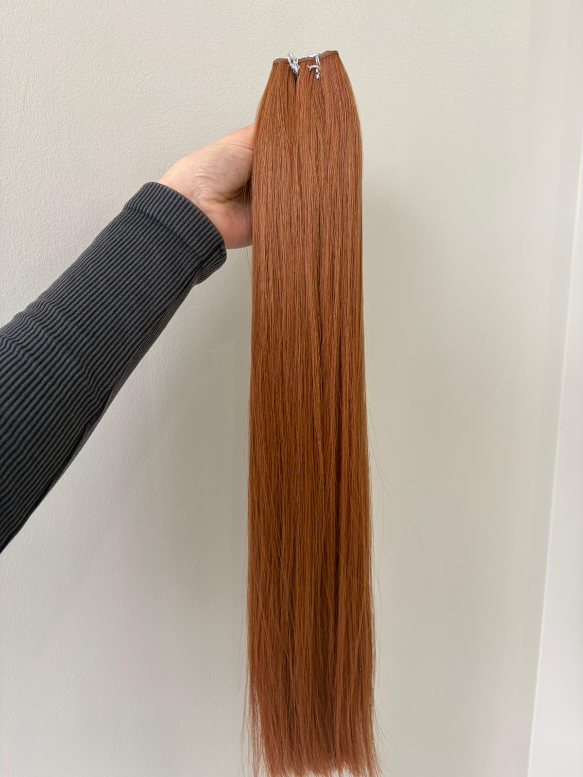 Orange hair extensions held by a person against a neutral background