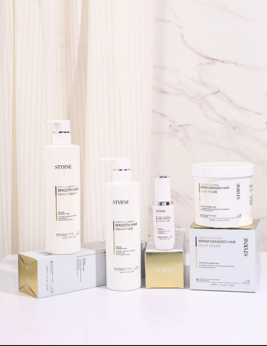 Collection of Styrne hair care products on a white surface with a marble wall background.