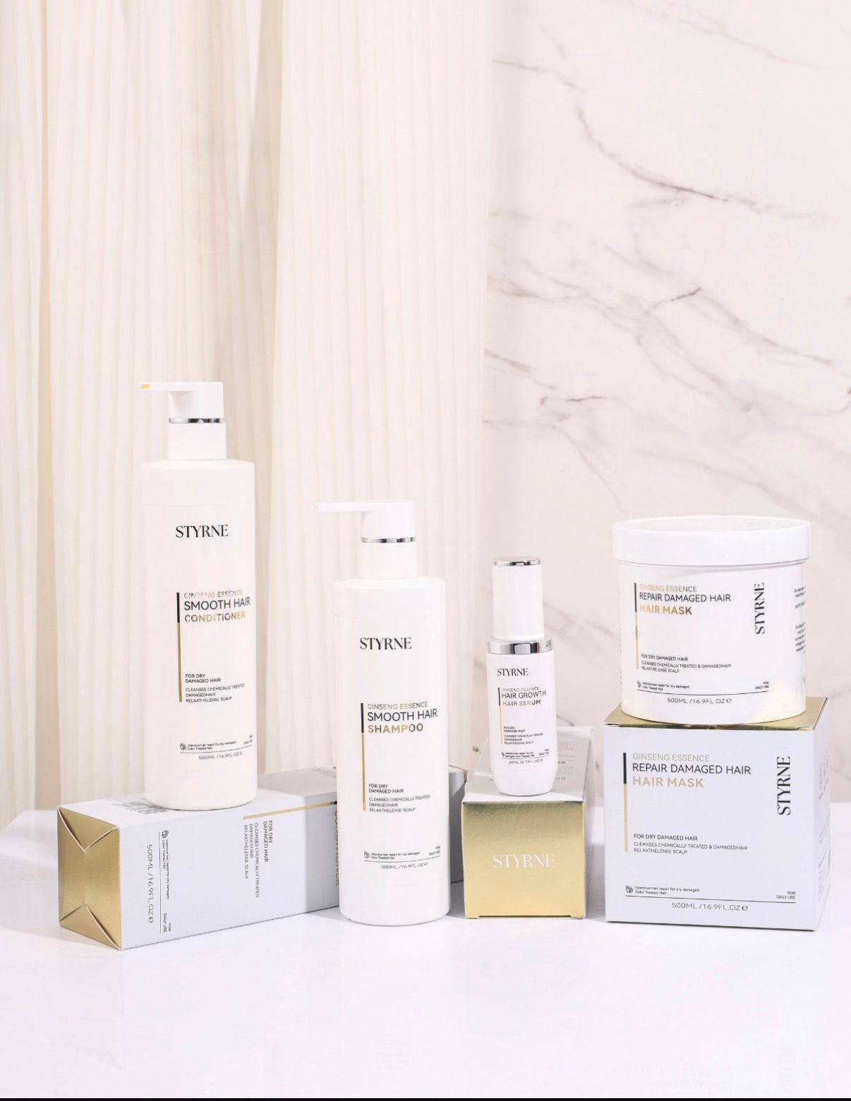 Collection of Styrne hair care products on a white surface with a marble wall background.