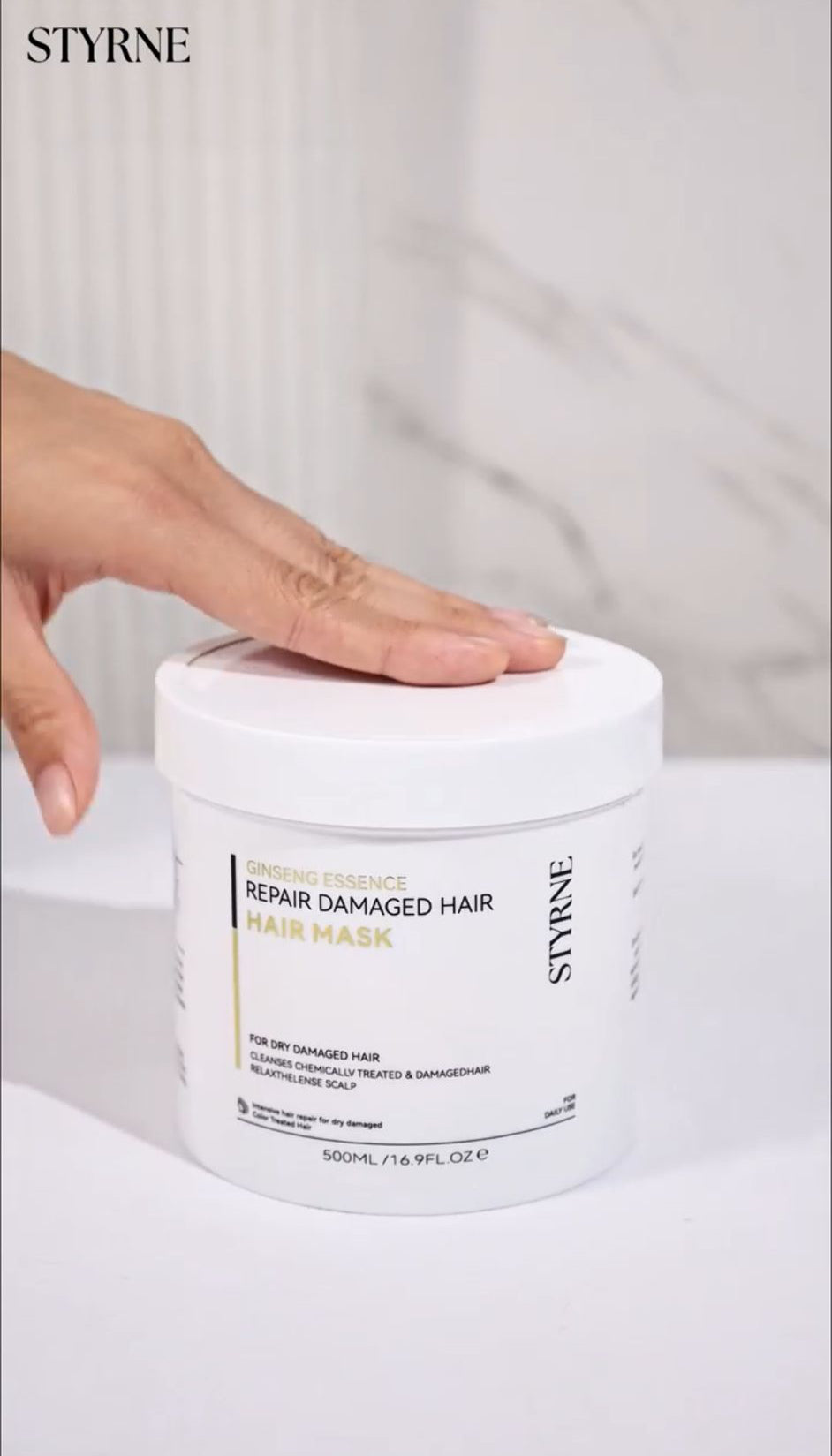 Styrne hair mask jar with a hand on top against a white background