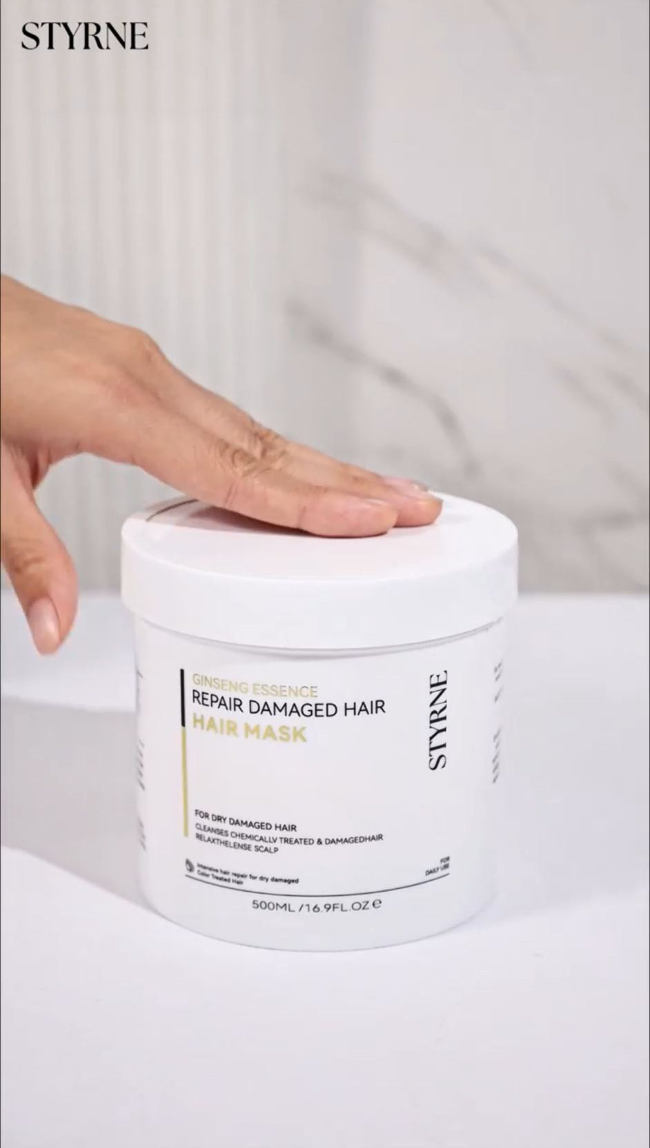 Styrene hair mask jar with a hand on top against a white background