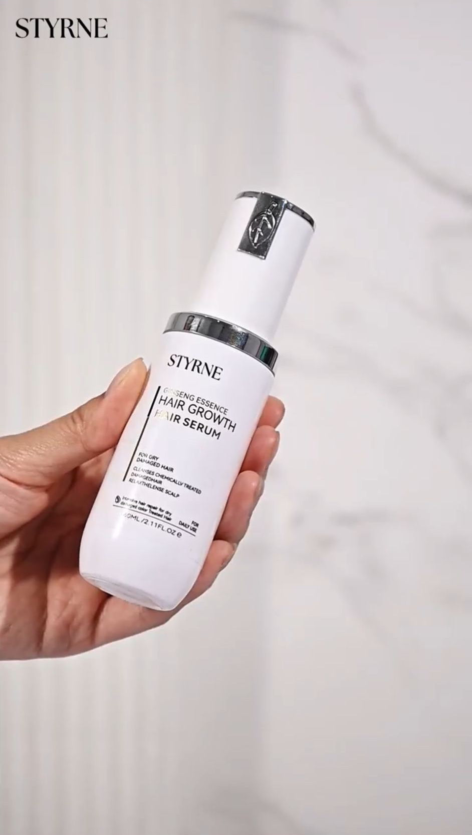 Hand holding a white serum bottle labeled 'STYRNE' against a plain background