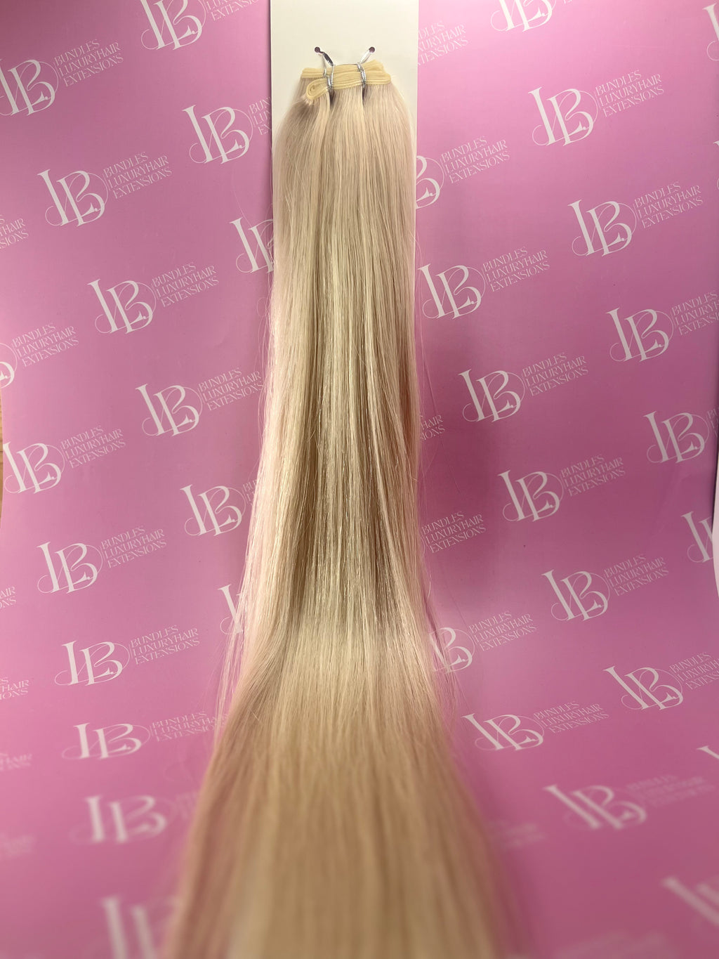 Blonde hair extensions on a stand against a pink background with 'IB' branding.