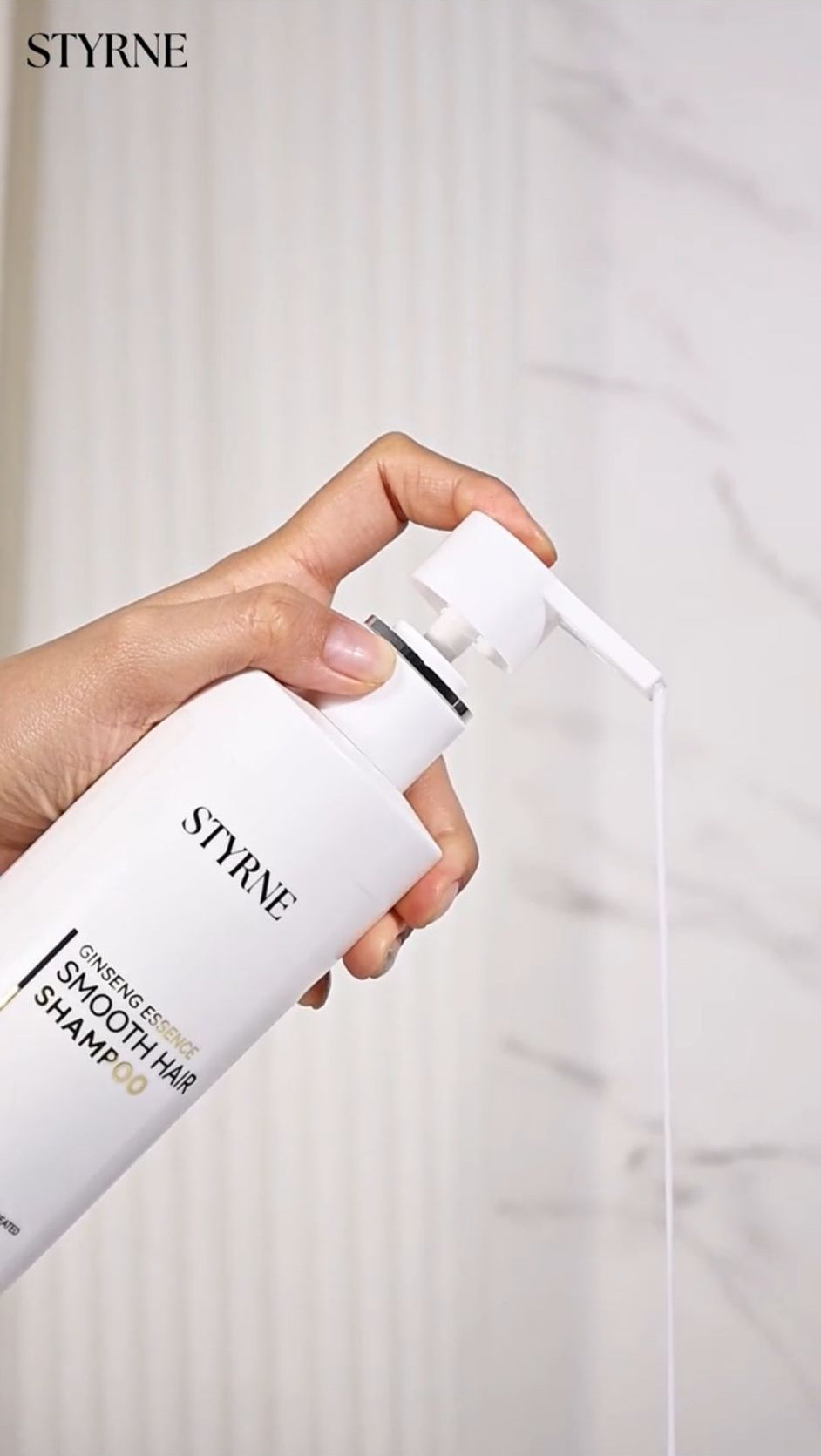 Hand holding a bottle of STYRNE shampoo with a white background