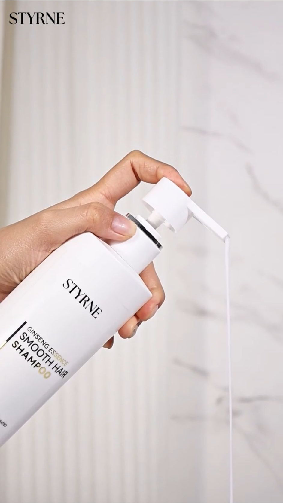 Hand holding a bottle of STYRNE shampoo with a white background
