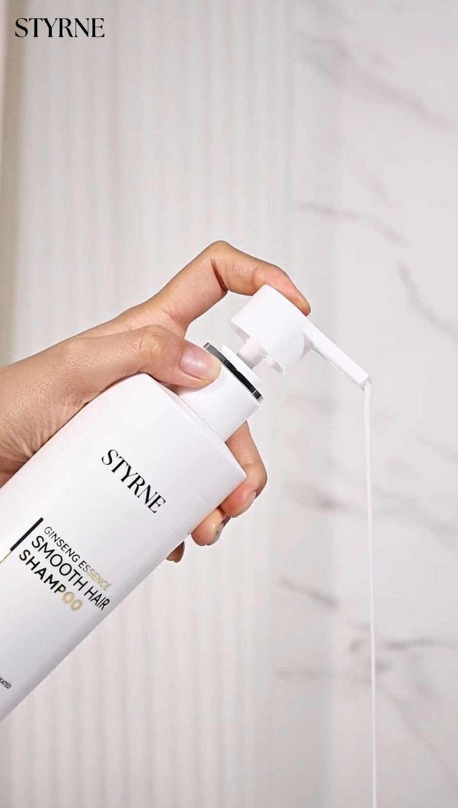 Hand holding a bottle of STYRNE shampoo with a white background