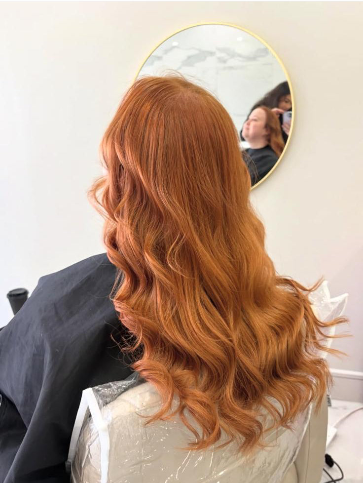 Person with long, wavy red hair sitting in a chair, shown on a smartphone screen.