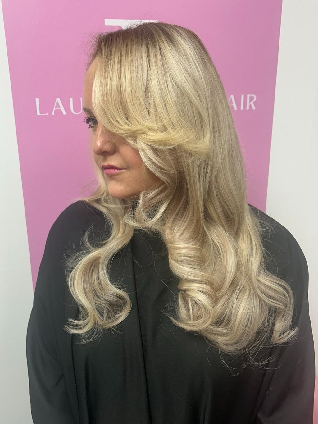 Woman with long blonde hair in front of a pink background with 'Laura Byrne Hair' branding.
