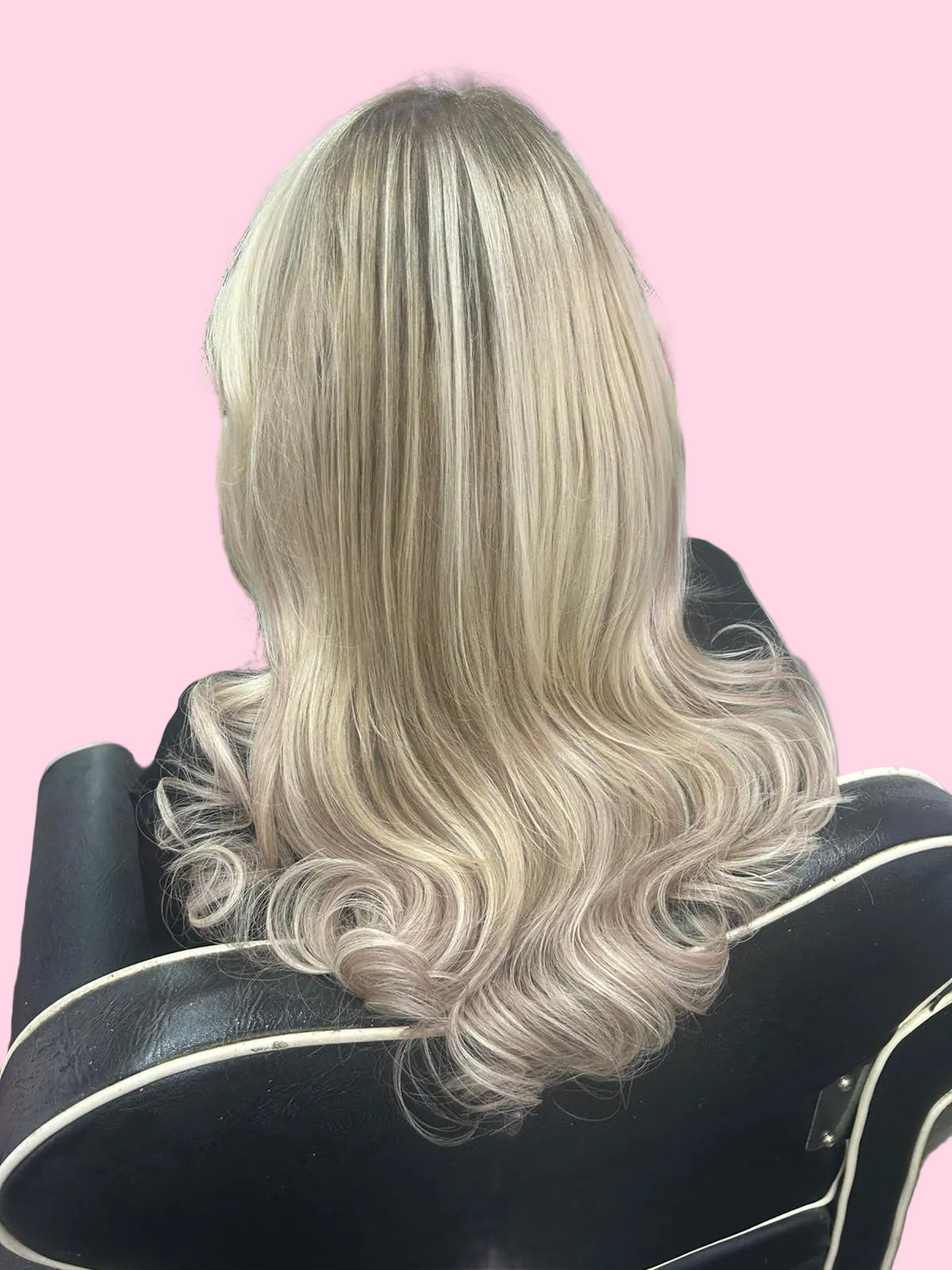 Blonde wavy hair styled in a salon setting with flowers and people in the background.